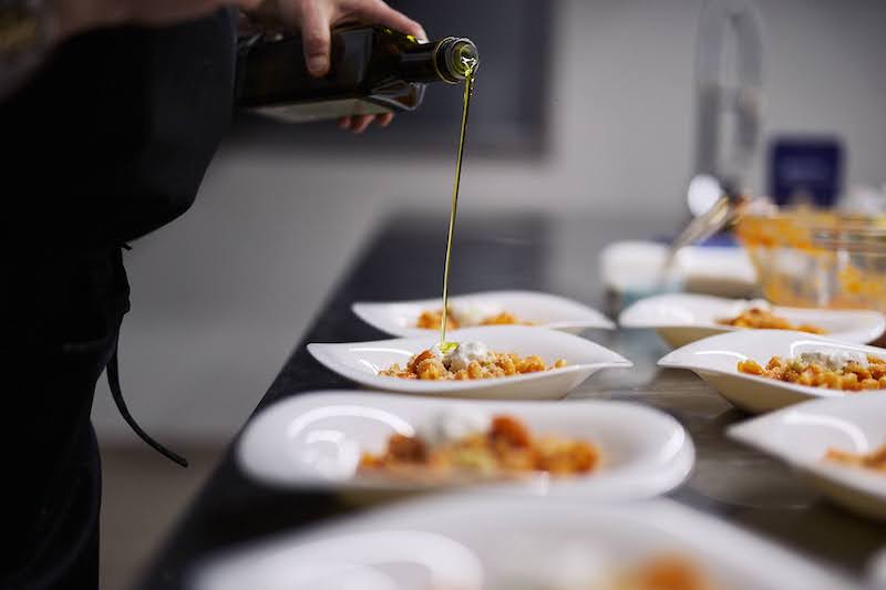 Tavola con piatti di pasta e persona che versa olio extravergine di oliva