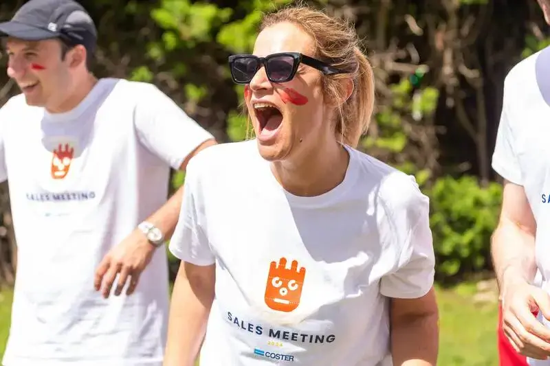 Ragazza con tshirt bianca e occhiali da sole che urla e altre due persone con maglia bianca che si sfidano