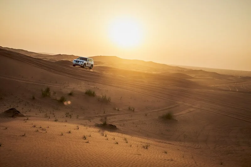 Jeep che viaggia sulle dune del deserto con il sole che brilla nel cielo