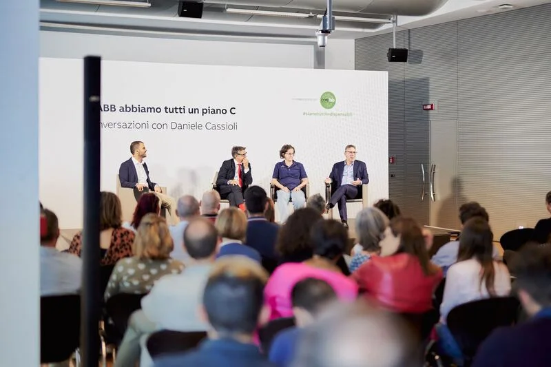 Persone sul palco durante una conferenza con pubblico seduto nella sala