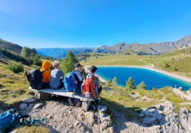 Ragazzi seduti su una panchina di legno che ammirano un lago di montagna