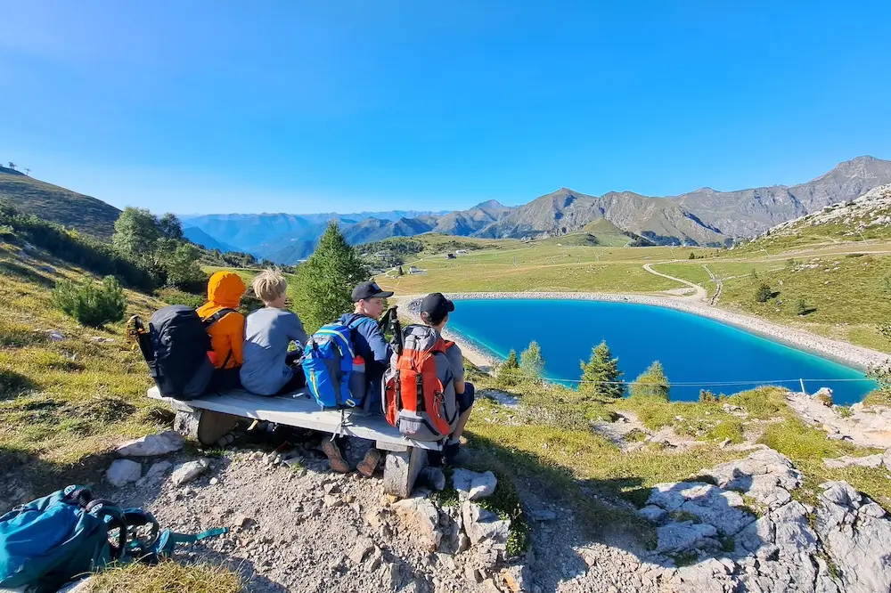 Ragazzi seduti su una panchina di legno che ammirano un lago di montagna