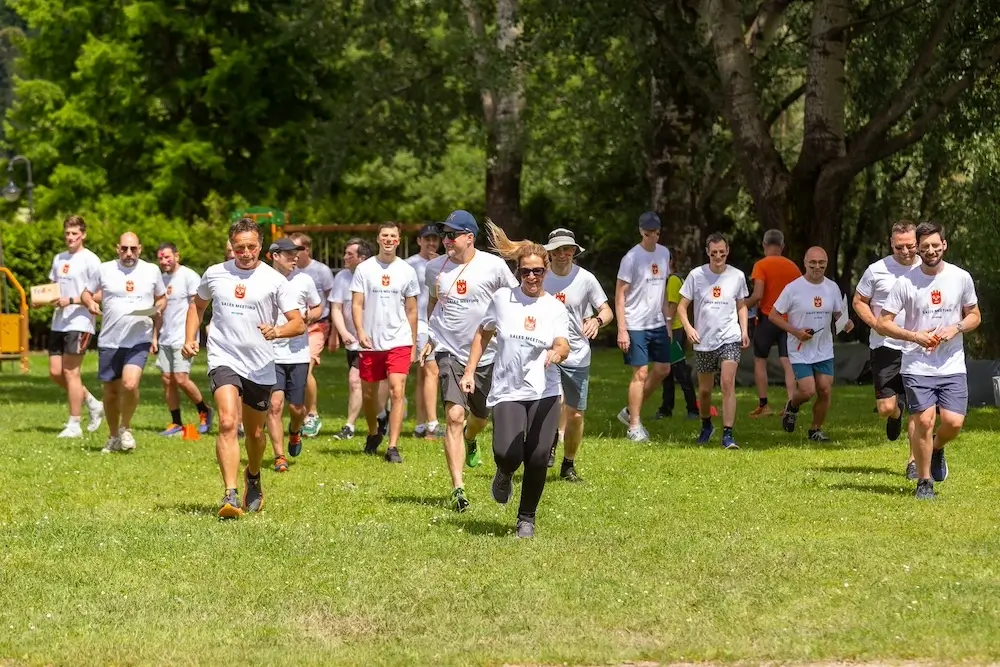 Dipendenti aziendali che partecipano a una corsa di team building in un parco verde in Lombardia, indossando magliette personalizzate.