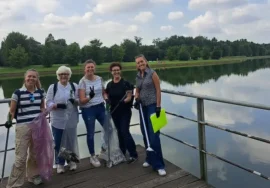 Gruppo aziendale sorridente posa con i sacchi raccolti dopo una giornata di team building ecologico e solidale al Parco Nord, con vista sul lago.
