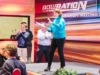 Manager con maglione azzurro che parla sorridente sul palco durante un kick-off aziendale a Milano