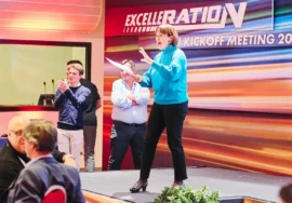 Manager con maglione azzurro che parla sorridente sul palco durante un kick-off aziendale a Milano