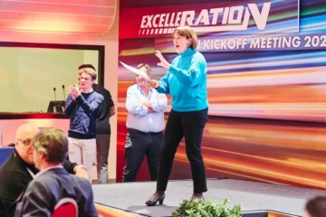 Manager con maglione azzurro che parla sorridente sul palco durante un kick-off aziendale a Milano