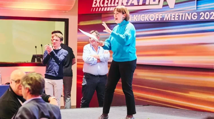 Manager con maglione azzurro che parla sorridente sul palco durante un kick-off aziendale a Milano