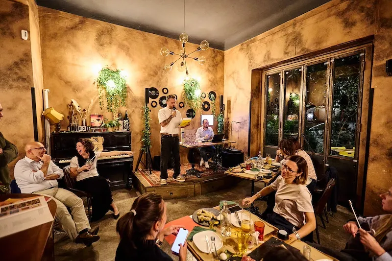 Sala evento dove presentatore pone domande al pubblico seduto in sala