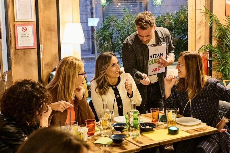 Presentatore con cartellina porge il microfono alla partecipante e alle sue colleghe per dare la risposta