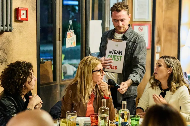 Presentatore con cartellina porge il microfono alla partecipante per dare la risposta
