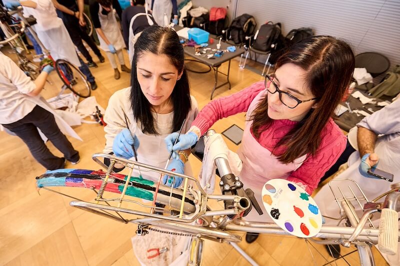 Due collaboratrici fanno squadra e applicano creatività e cura nella verniciatura del portapacchi della bicicletta, durante il Team Building in Italia (ABB).