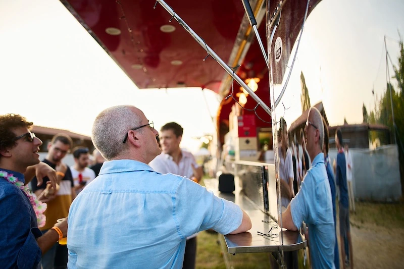 Food truck allestito per catering durante un summer party aziendale con partecipanti che ordinano cibo all’aperto