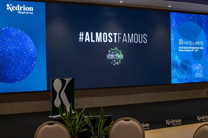 Sala conferenze allestita per team building aziendale AlmostFamous con schermi e branding Kedrion a Roma
